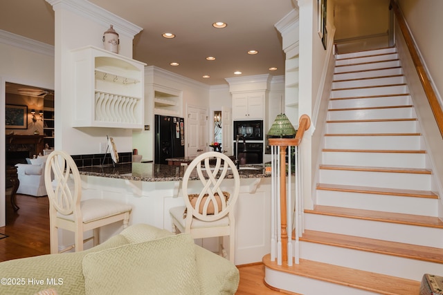 kitchen featuring light wood-style flooring, black appliances, ornamental molding, dark stone counters, and open shelves