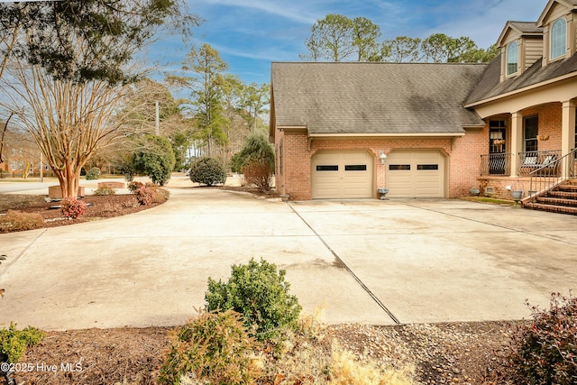 view of property exterior with driveway, brick siding, an attached garage, and a shingled roof