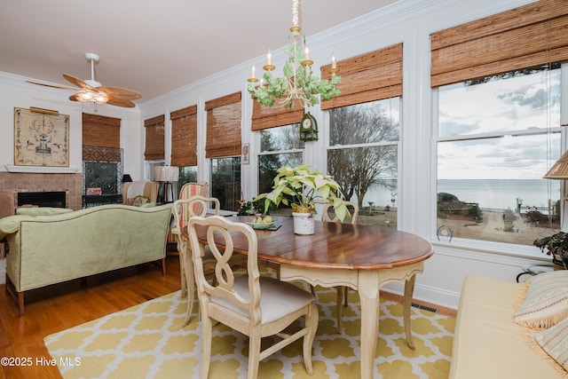 dining area with visible vents, wood finished floors, crown molding, a fireplace, and ceiling fan with notable chandelier