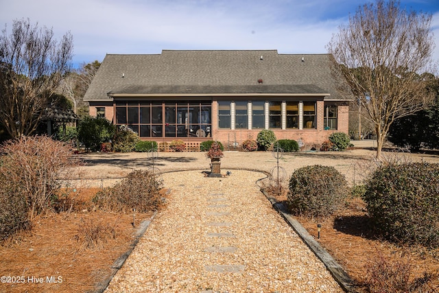 rear view of property with brick siding, a shingled roof, and a sunroom