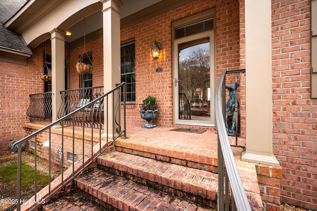 entrance to property featuring a shingled roof, a porch, and brick siding