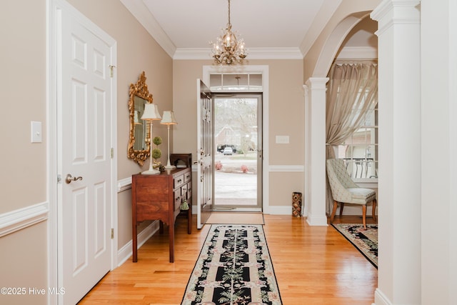 entryway featuring arched walkways, crown molding, light wood-style floors, decorative columns, and an inviting chandelier