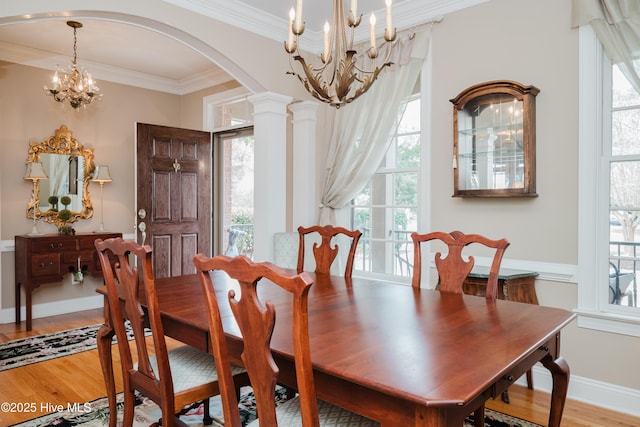 dining space with a chandelier, arched walkways, light wood-style flooring, decorative columns, and crown molding