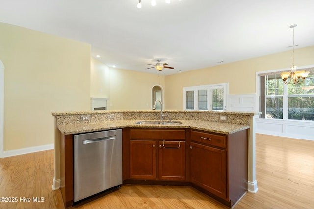 kitchen with light wood finished floors, brown cabinets, decorative light fixtures, a sink, and stainless steel dishwasher