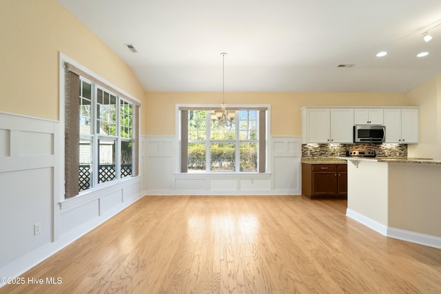 unfurnished dining area with a notable chandelier, lofted ceiling, visible vents, a decorative wall, and light wood-style floors