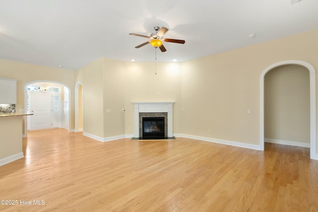 unfurnished living room featuring arched walkways, a fireplace, and light wood-style flooring