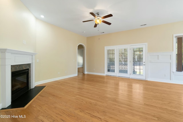 unfurnished living room with light wood-style floors, a glass covered fireplace, ceiling fan, and arched walkways