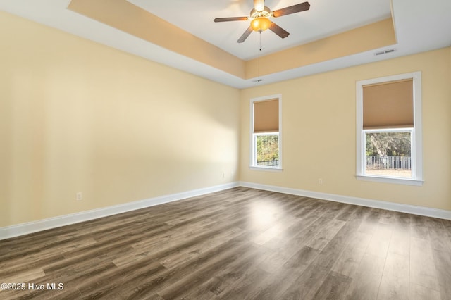 spare room featuring baseboards, visible vents, a tray ceiling, and wood finished floors