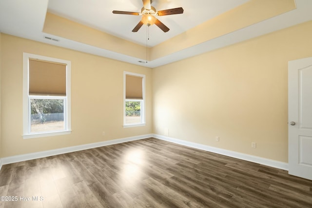 unfurnished room featuring dark wood-style floors, a tray ceiling, visible vents, ceiling fan, and baseboards