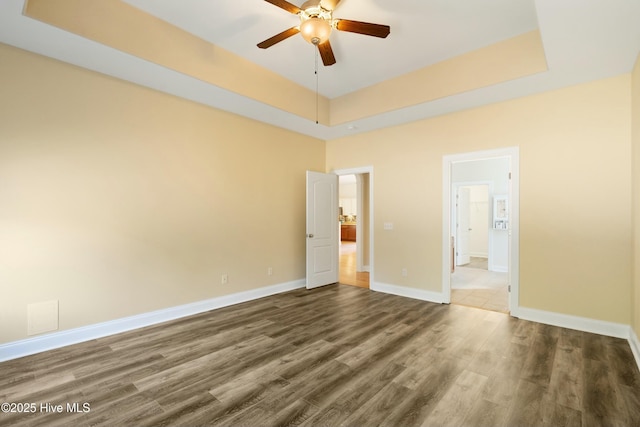 unfurnished bedroom with a ceiling fan, a raised ceiling, baseboards, and dark wood-style flooring