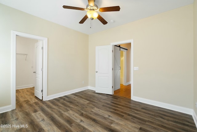 unfurnished bedroom with a barn door, baseboards, dark wood-type flooring, a walk in closet, and a closet