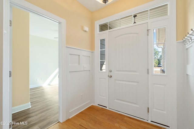 foyer entrance featuring light wood finished floors, baseboards, and a wainscoted wall