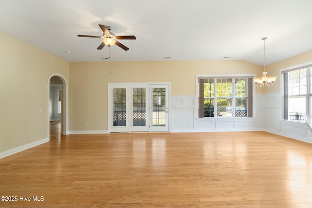 unfurnished living room with light wood-style floors, arched walkways, vaulted ceiling, and ceiling fan with notable chandelier