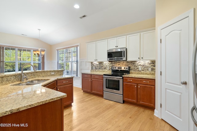 kitchen with stainless steel appliances, a sink, white cabinets, brown cabinetry, and pendant lighting