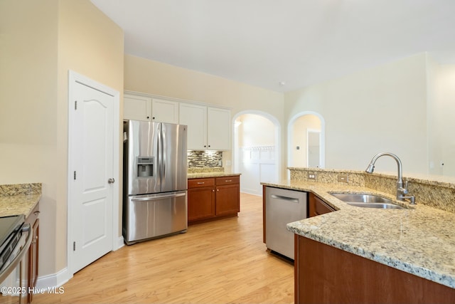 kitchen featuring brown cabinetry, light stone counters, stainless steel appliances, white cabinetry, and a sink