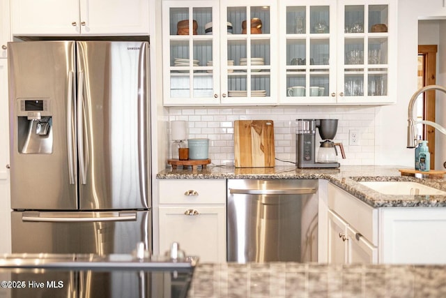 kitchen featuring stainless steel appliances, glass insert cabinets, white cabinets, a sink, and dark stone counters