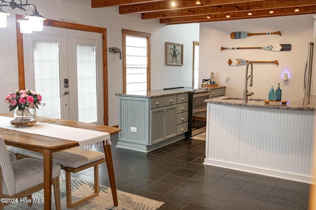 kitchen with a sink, french doors, gray cabinets, light stone countertops, and beamed ceiling