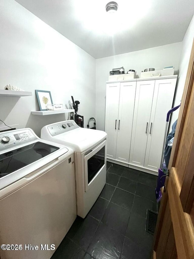 washroom with dark tile patterned flooring, separate washer and dryer, cabinet space, and visible vents