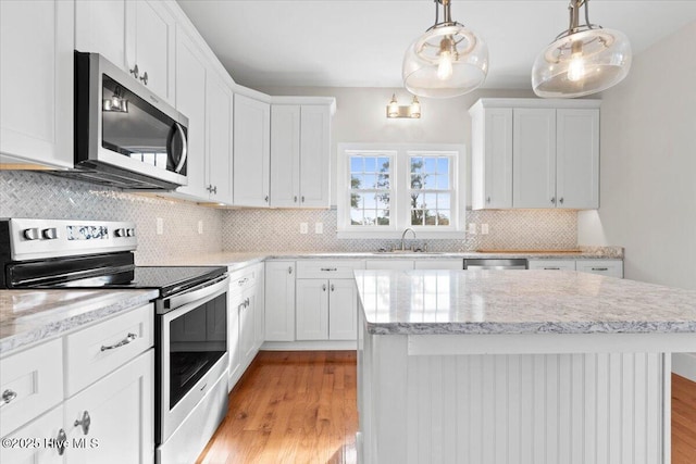 kitchen featuring decorative light fixtures, appliances with stainless steel finishes, white cabinets, a sink, and a kitchen island