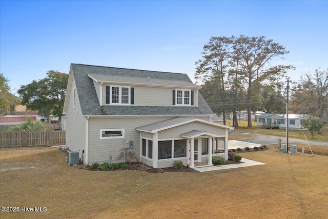 view of front facade featuring a shingled roof, a front yard, a sunroom, central AC, and fence