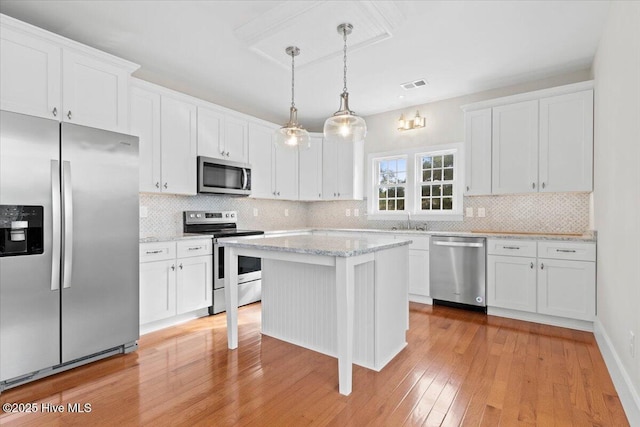 kitchen featuring visible vents, stainless steel appliances, white cabinetry, and decorative light fixtures