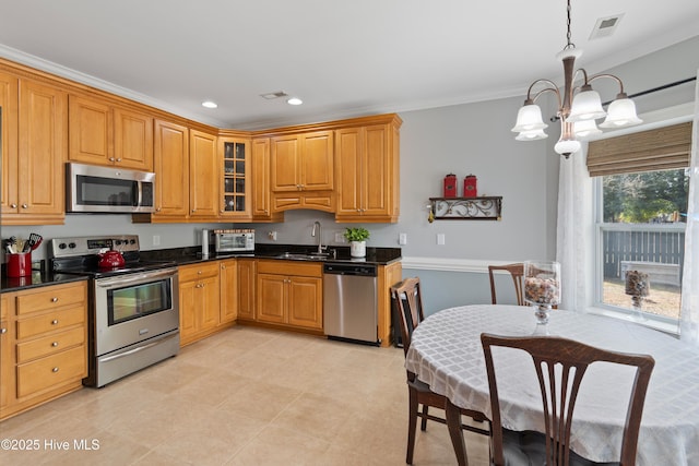 kitchen featuring dark countertops, glass insert cabinets, stainless steel appliances, pendant lighting, and a sink