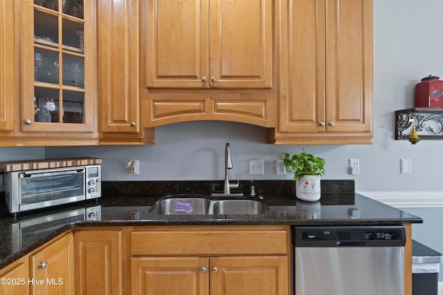 kitchen featuring brown cabinetry, glass insert cabinets, dark stone countertops, stainless steel dishwasher, and a sink