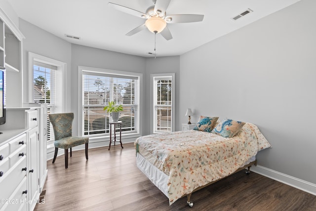 bedroom with a ceiling fan, visible vents, baseboards, and wood finished floors