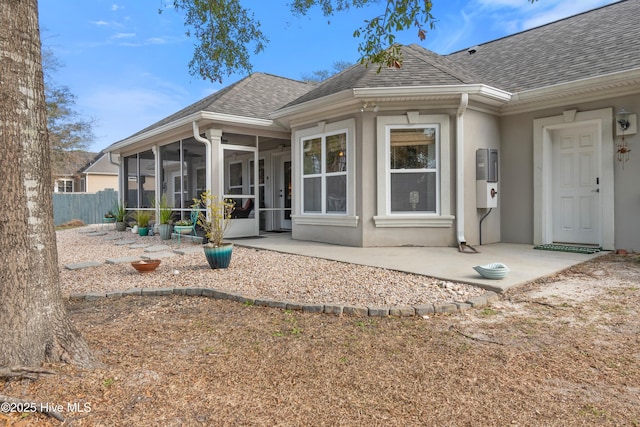 rear view of house with roof with shingles, a patio area, a sunroom, and stucco siding