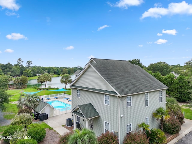 view of side of property featuring a fenced in pool, roof with shingles, central air condition unit, a water view, and fence