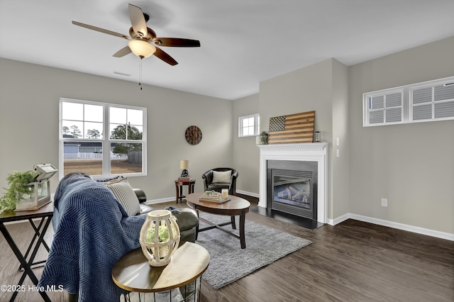 living room featuring a fireplace with flush hearth, wood finished floors, visible vents, and baseboards