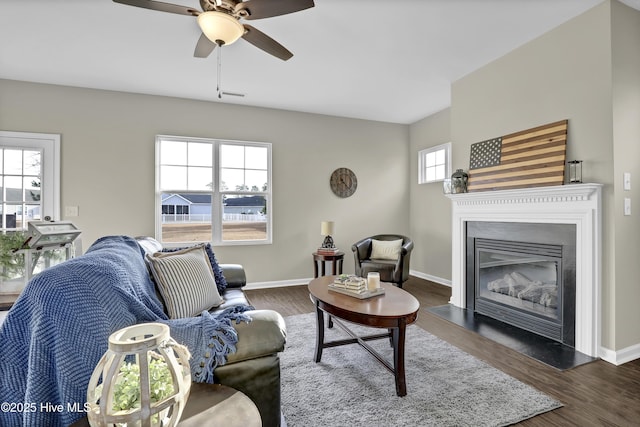 living area featuring ceiling fan, baseboards, wood finished floors, and a glass covered fireplace