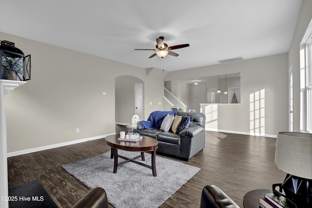 living area with arched walkways, dark wood-style flooring, visible vents, a ceiling fan, and baseboards