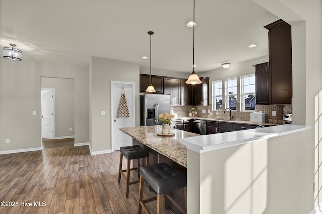 kitchen with tasteful backsplash, stainless steel appliances, dark brown cabinets, a kitchen bar, and a sink