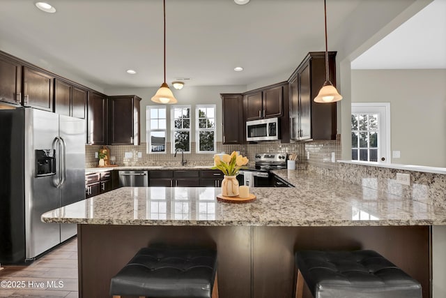 kitchen featuring stainless steel appliances, dark brown cabinets, a peninsula, and backsplash