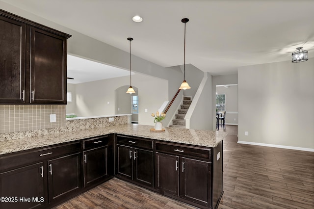 kitchen with dark wood-style floors, a peninsula, tasteful backsplash, and light stone counters