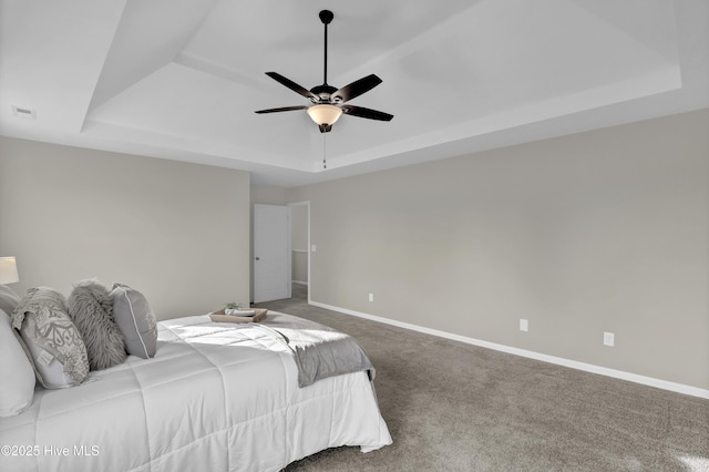 carpeted bedroom with a ceiling fan, a raised ceiling, and baseboards