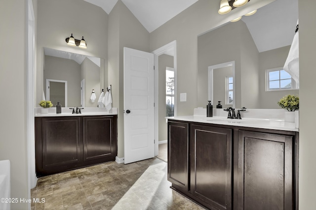 bathroom with vaulted ceiling, two vanities, and a sink