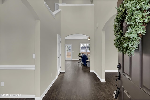 foyer entrance with dark wood-style floors, arched walkways, ceiling fan, and baseboards