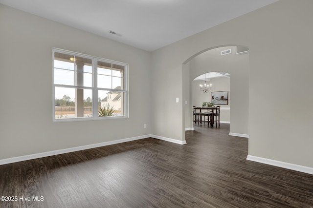 empty room featuring arched walkways, visible vents, dark wood finished floors, and baseboards