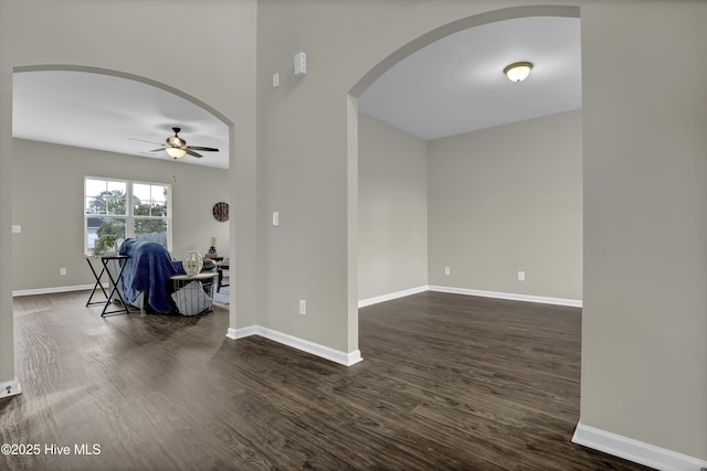 spare room with arched walkways, dark wood-style floors, and baseboards