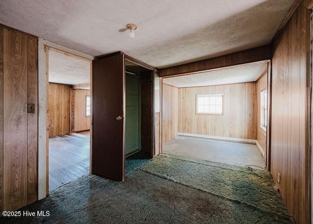 hall with carpet, wooden walls, and a textured ceiling