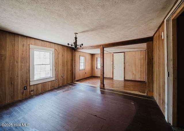 empty room with dark wood-style floors, a chandelier, a textured ceiling, and wood walls