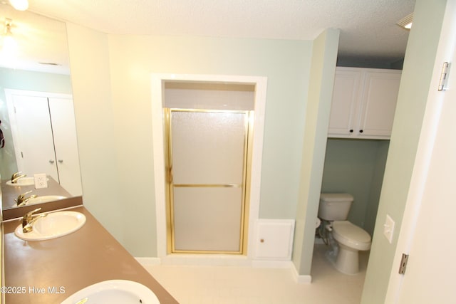 bathroom featuring a textured ceiling, toilet, a sink, double vanity, and a stall shower