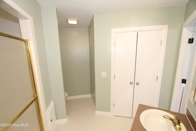 full bathroom with baseboards, toilet, a shower with door, a textured ceiling, and a sink