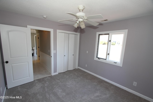 unfurnished bedroom featuring a textured ceiling, carpet floors, visible vents, baseboards, and a closet