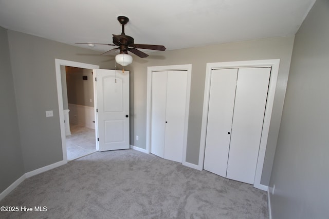 unfurnished bedroom featuring multiple closets, carpet, baseboards, and a ceiling fan