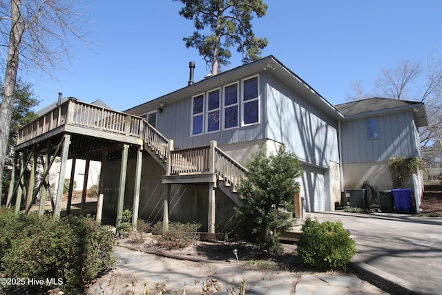 rear view of house with stairway, an attached garage, central AC unit, driveway, and a wooden deck