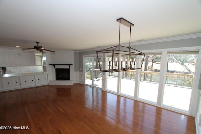 unfurnished living room featuring a fireplace with raised hearth, ceiling fan with notable chandelier, wood finished floors, and crown molding