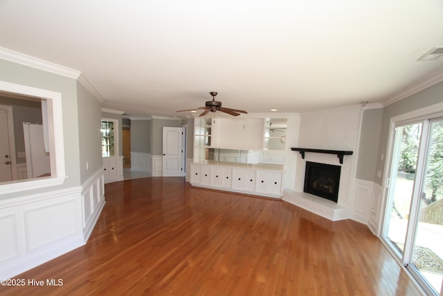 unfurnished living room featuring visible vents, wood finished floors, crown molding, a fireplace, and a decorative wall